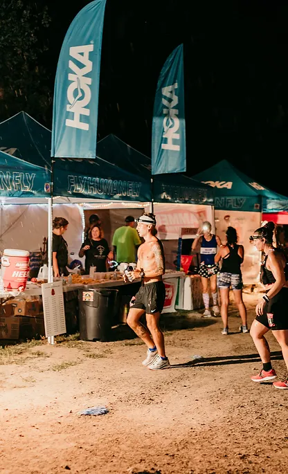Runners visit the aid station adorned with HOKA banners at the Anchor Down Ultra Marathon, stocked with various nutrition and hydration options.